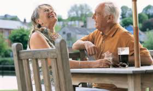A woman and a man sitting by a table in the open, laughing.